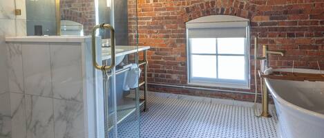 Une salle de bain moderne avec une douche à parois de verre, un grand miroir, une baignoire et un mur en briques.