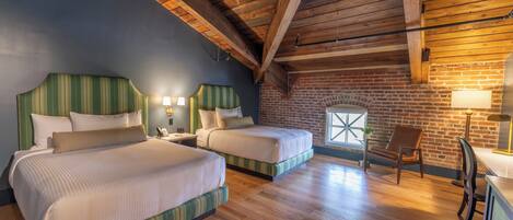 A room with two beds, wooden floors, a brick wall, and a window.