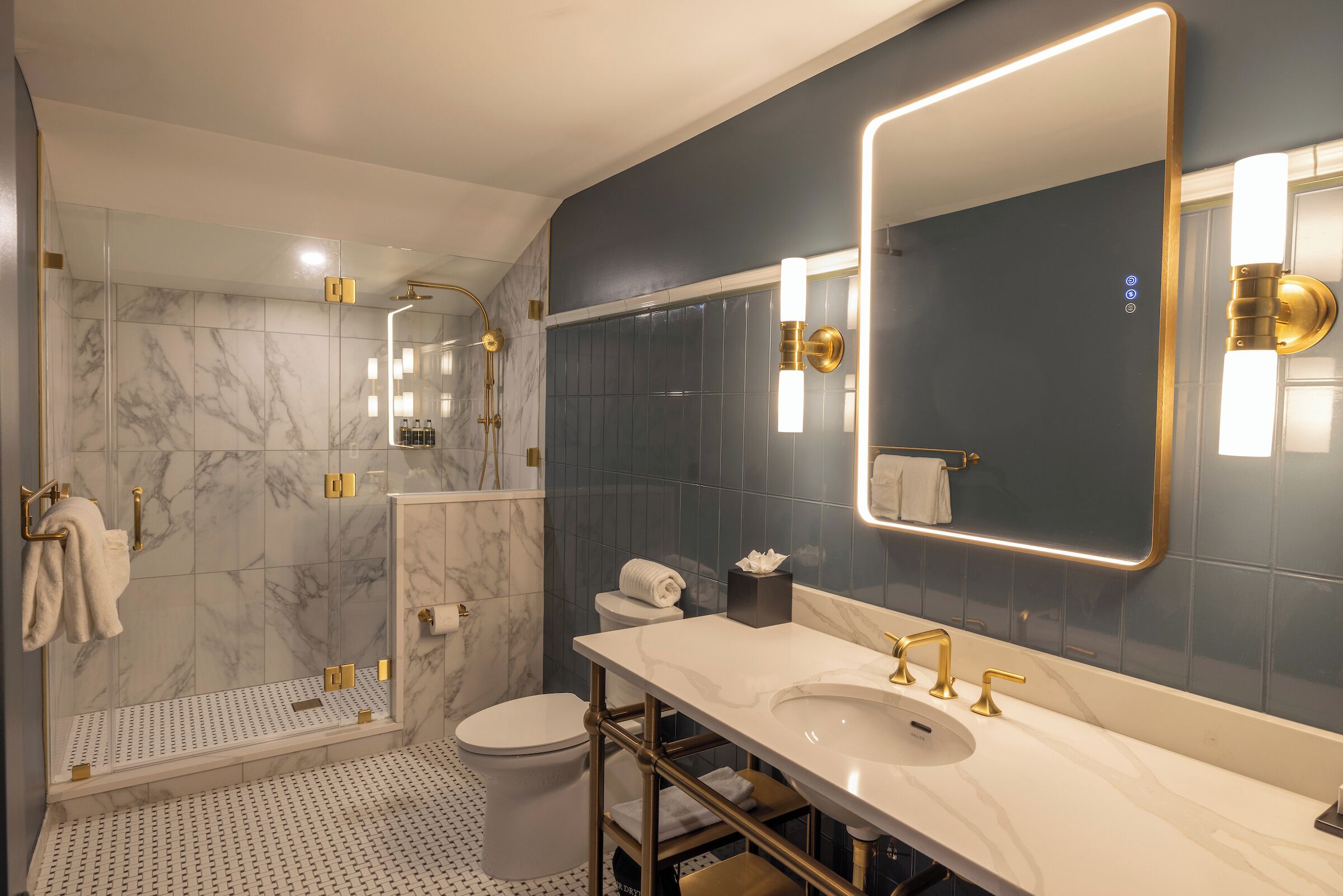 A modern bathroom with a shower, toilet, and vanity with a large mirror and gold fixtures.