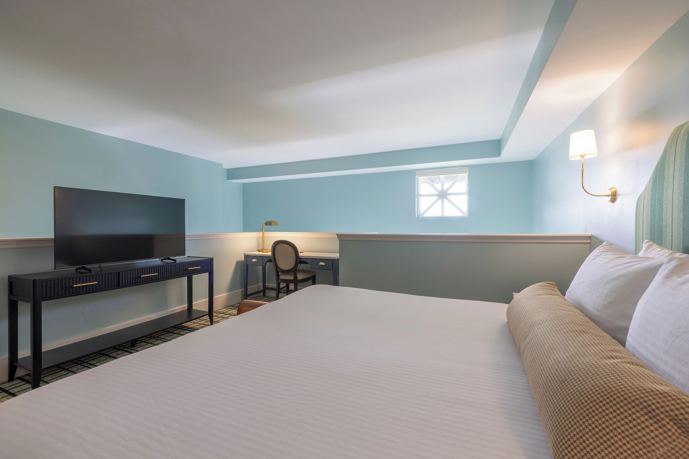 Een hotelkamer met een bed, een bureau met stoel, een televisie en een raam.