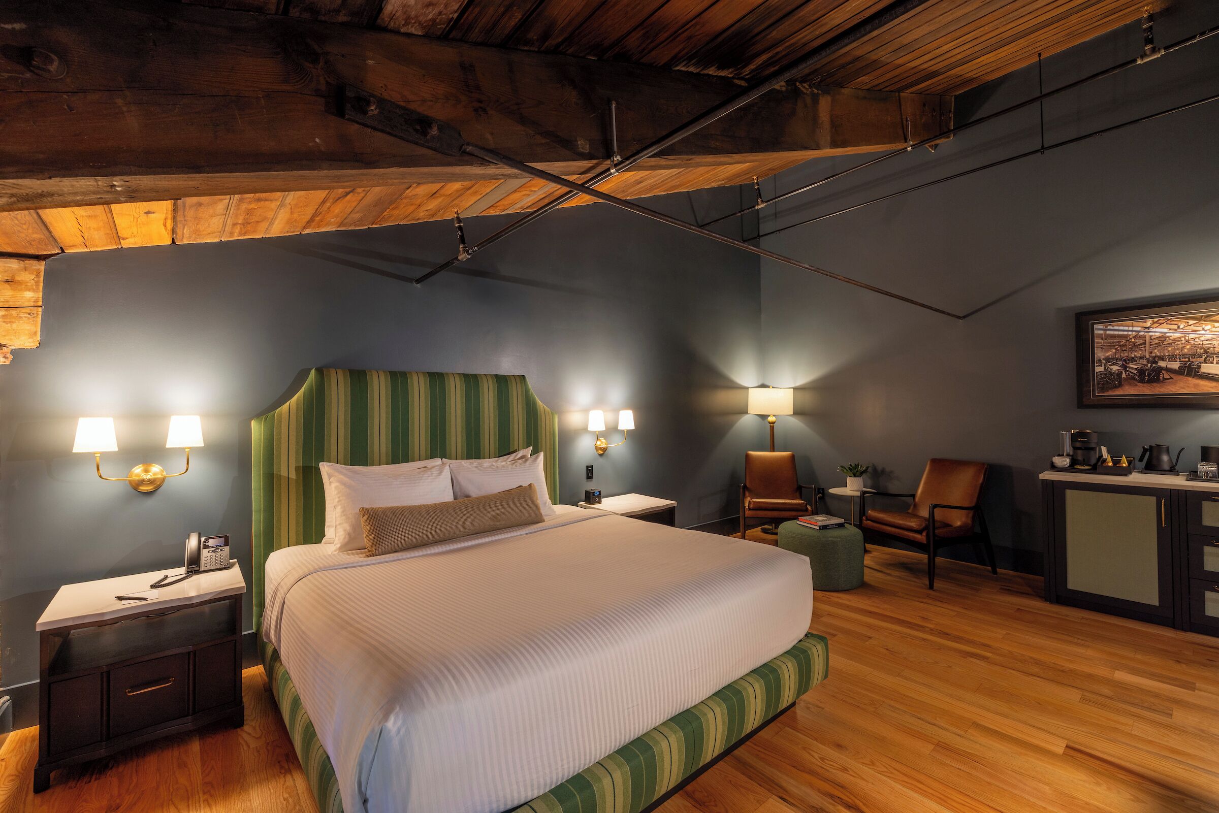 A hotel room with a bed, bedside tables, a desk, a chair, and a kitchenette.