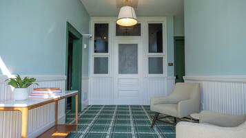 A hallway with a checkered floor, a white door, a chair, and a table with a plant and books.