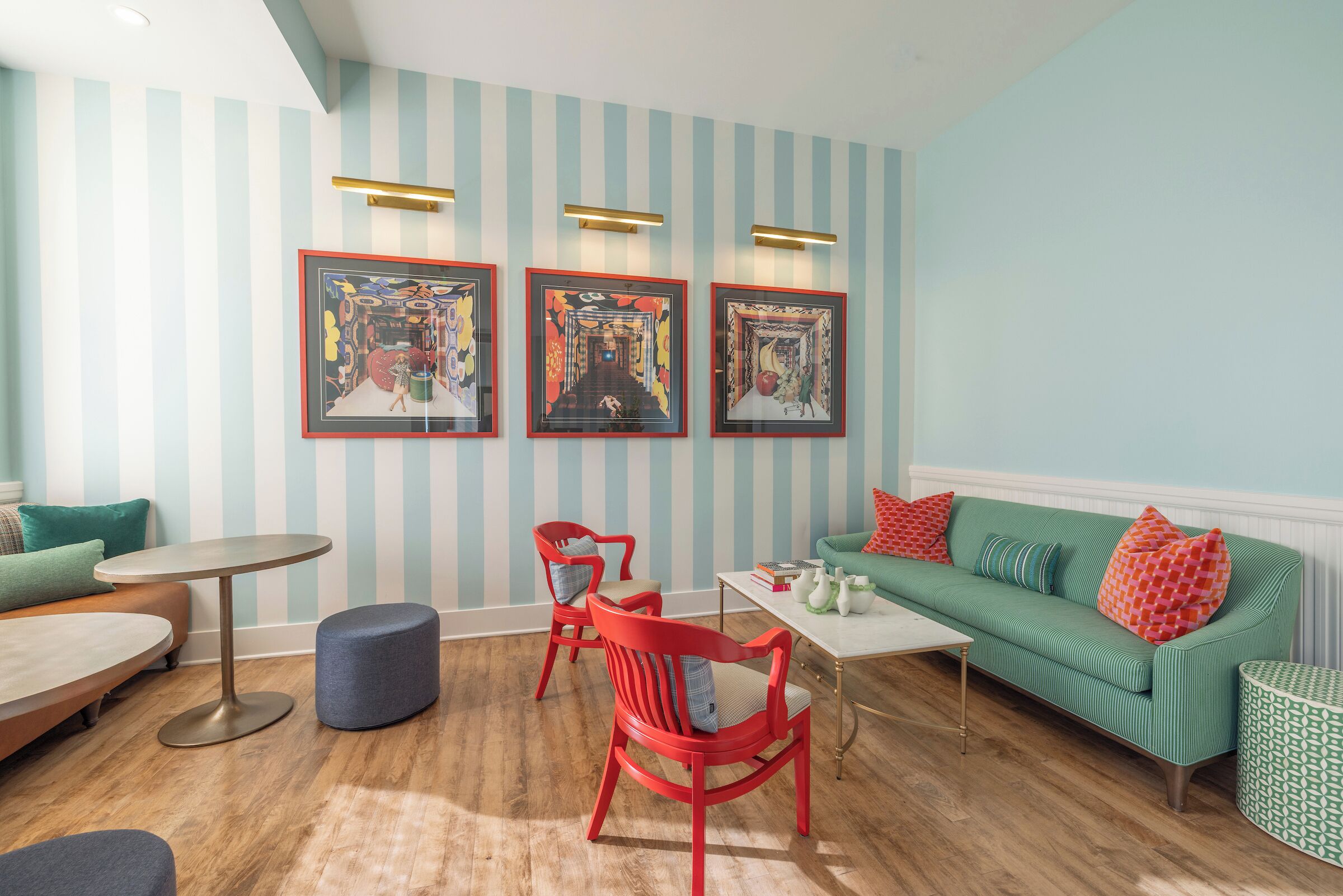Una habitación con paredes a rayas, un sofá verde, sillas rojas, una mesa redonda y cuadros en la pared.