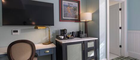 A room with a desk, chair, television, framed picture, lamp, and a door.