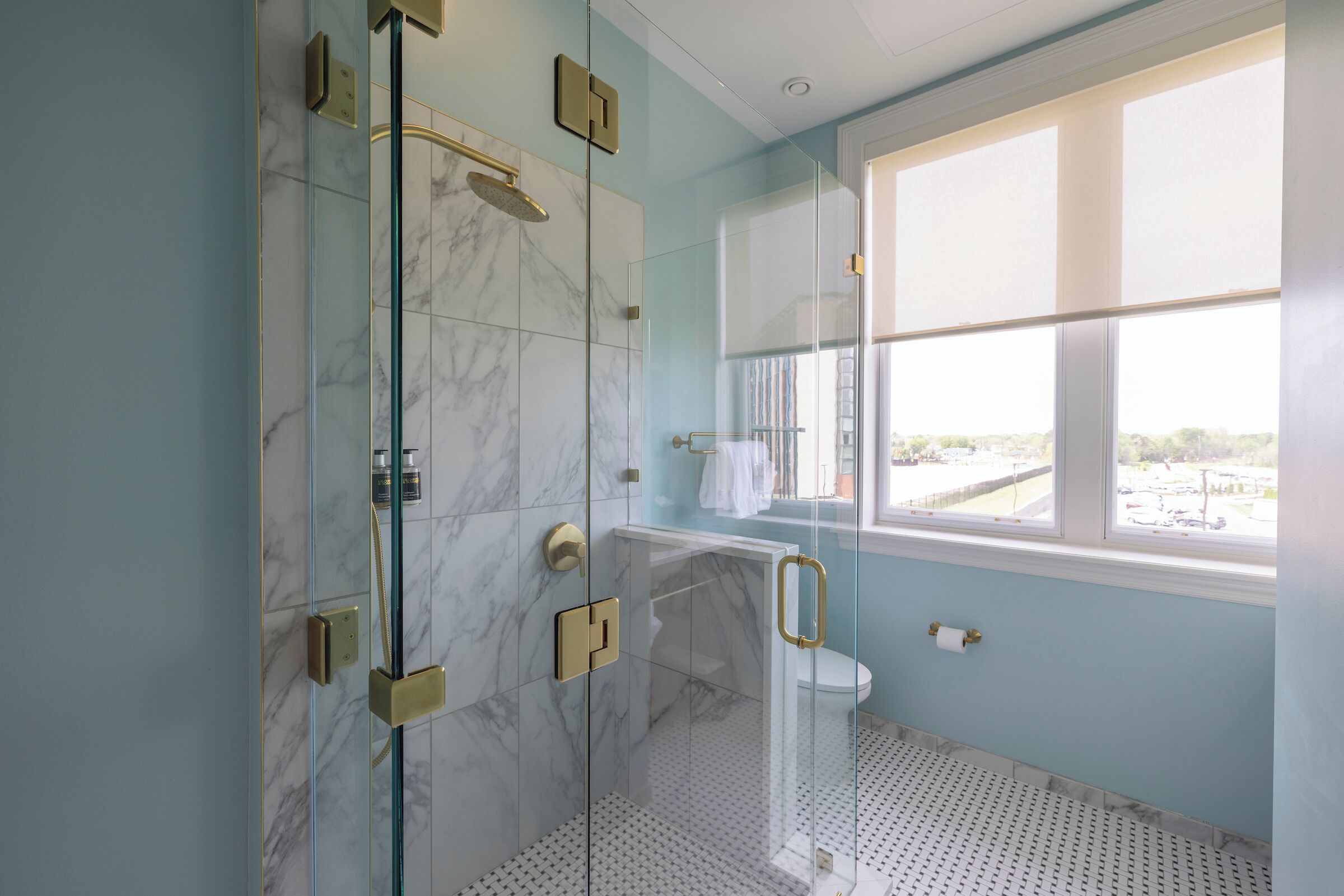 Une salle de bain dotée d’une douche à parois de verre, de murs en marbre, de toilettes et d’une fenêtre offrant une vue agréable.