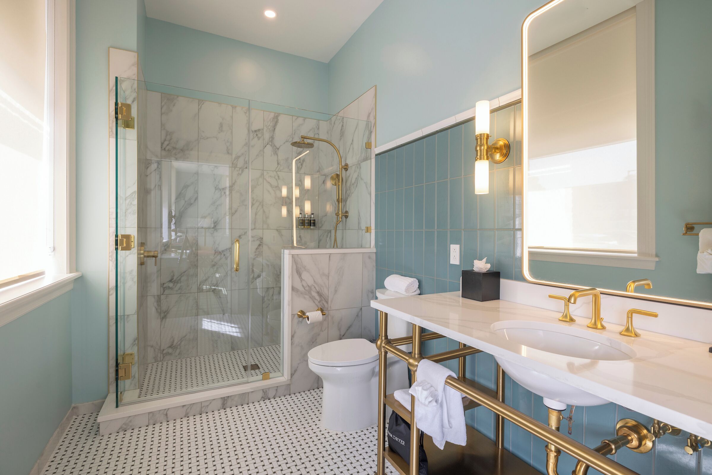 Un baño moderno con ducha envuelta en vidrio, inodoro blanco, tocador con lavamanos y detalles dorados, y un espejo grande.
