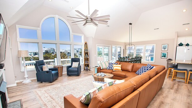 A spacious living room with a large sectional sofa, a fireplace, and a view of the outside. - Semi-Oceanfront, Ocean Views, Priv. Pool, Hot Tub-WL922, Beauty and the Beach (Corolla)