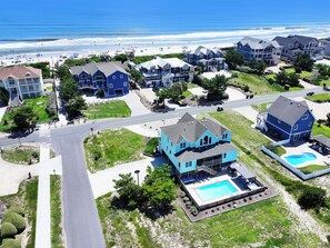 A coastal residential area with houses, a swimming pool, and a beach in the background. - Semi-Oceanfront, Ocean Views, Priv. Pool, Hot Tub-WL922, Beauty and the Beach (Corolla)