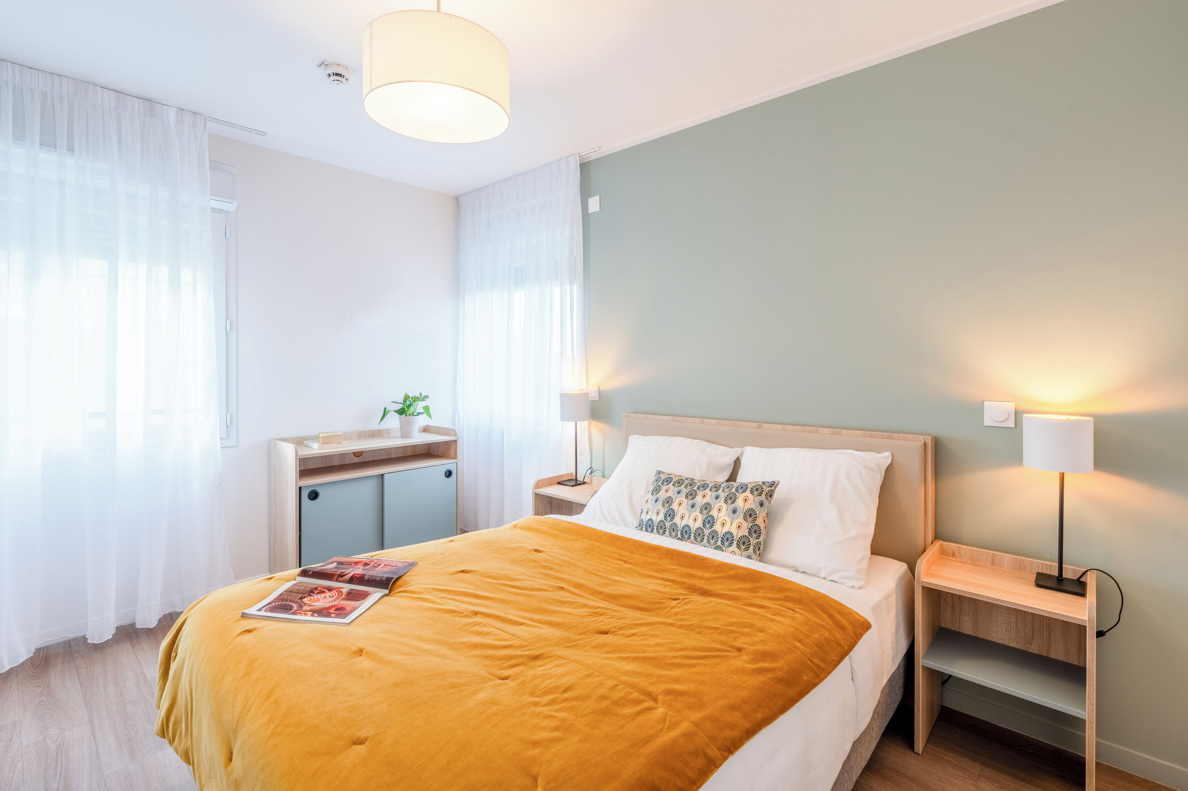 Et hotelværelse med seng, sengeborde, et skrivebord og en lampe.