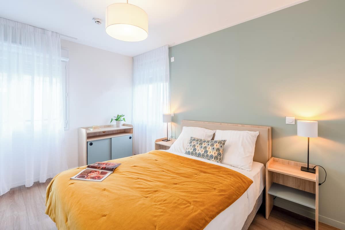 A hotel room with a bed, bedside tables, a desk, and a lamp.