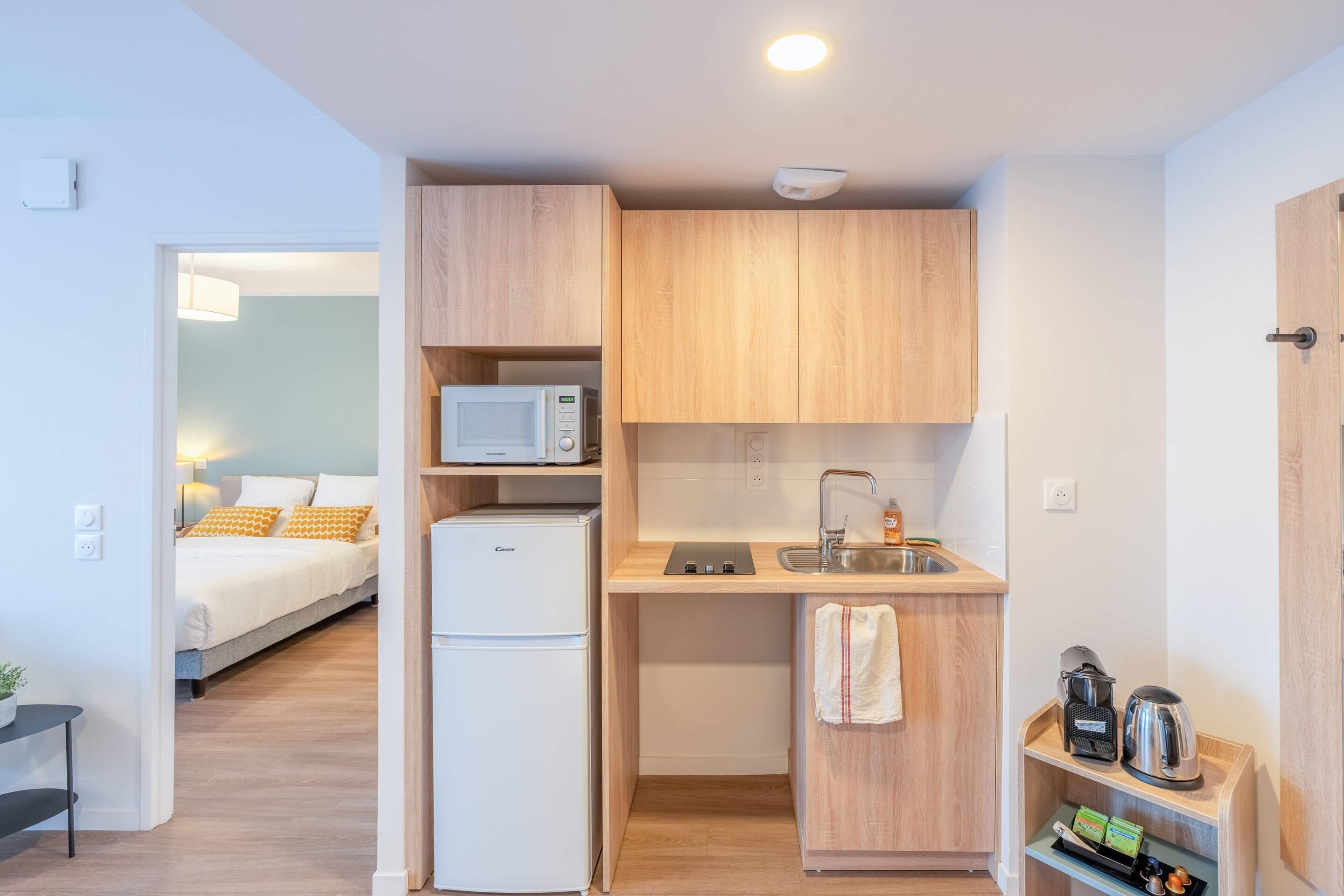 Eine kompakte Küchenzeile mit Mikrowelle, Kühlschrank, Spüle und Holzschränken.
