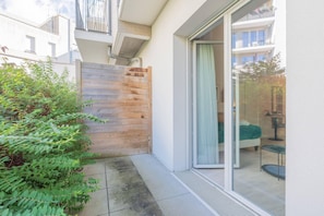 A modern apartment with a sliding glass door leading to a balcony, a wooden fence, and a small garden area. - Quality Aparthotel Moissy-Cramayel (Moissy-Cramayel)