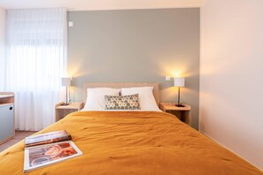A neatly made bed with a yellow bedspread, two bedside lamps, and a pillow with a blue and white pattern. - Quality Aparthotel Moissy-Cramayel (Moissy-Cramayel)