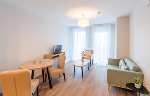 A modern living room with a sofa, a dining table with chairs, a TV, and a small side table with a plant. - Quality Aparthotel Moissy-Cramayel (Moissy-Cramayel)