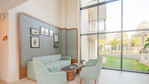 Un soggiorno moderno con un divano blu chiaro, due poltrone abbinate e un tavolino. Una parete decorativa con quadri incorniciati e un'ampia finestra che offre vista sull'esterno.