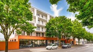 Un edificio moderno con fachada de vidrio, coches estacionados y árboles.