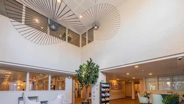 Un vestíbulo amplio con techo alto, un árbol en maceta en el centro, zonas de estar y una mesa de recepción.