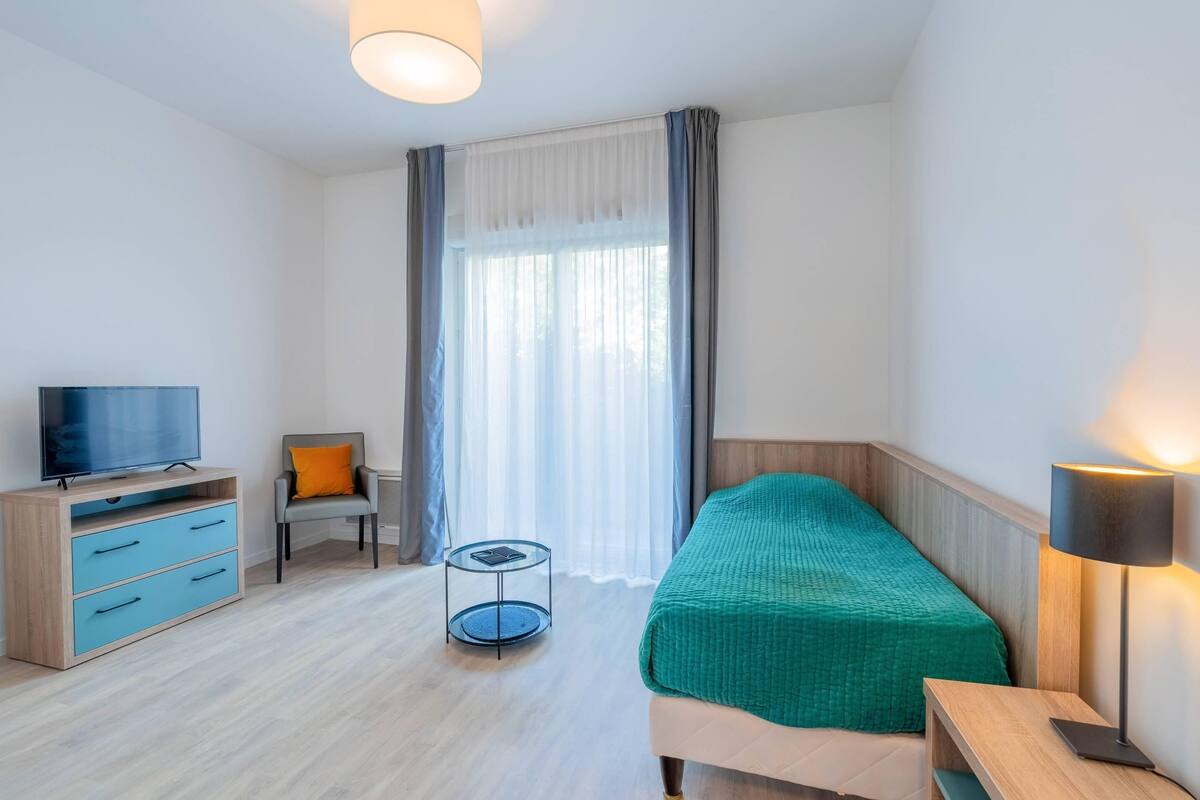 Habitació d'hotel amb un llit, un televisor, una cadira, una taula petita i una làmpada.