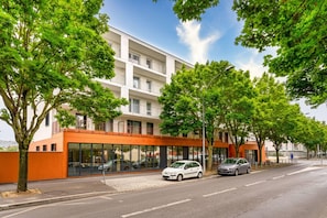 Un edificio moderno con fachada de vidrio, coches estacionados y árboles.