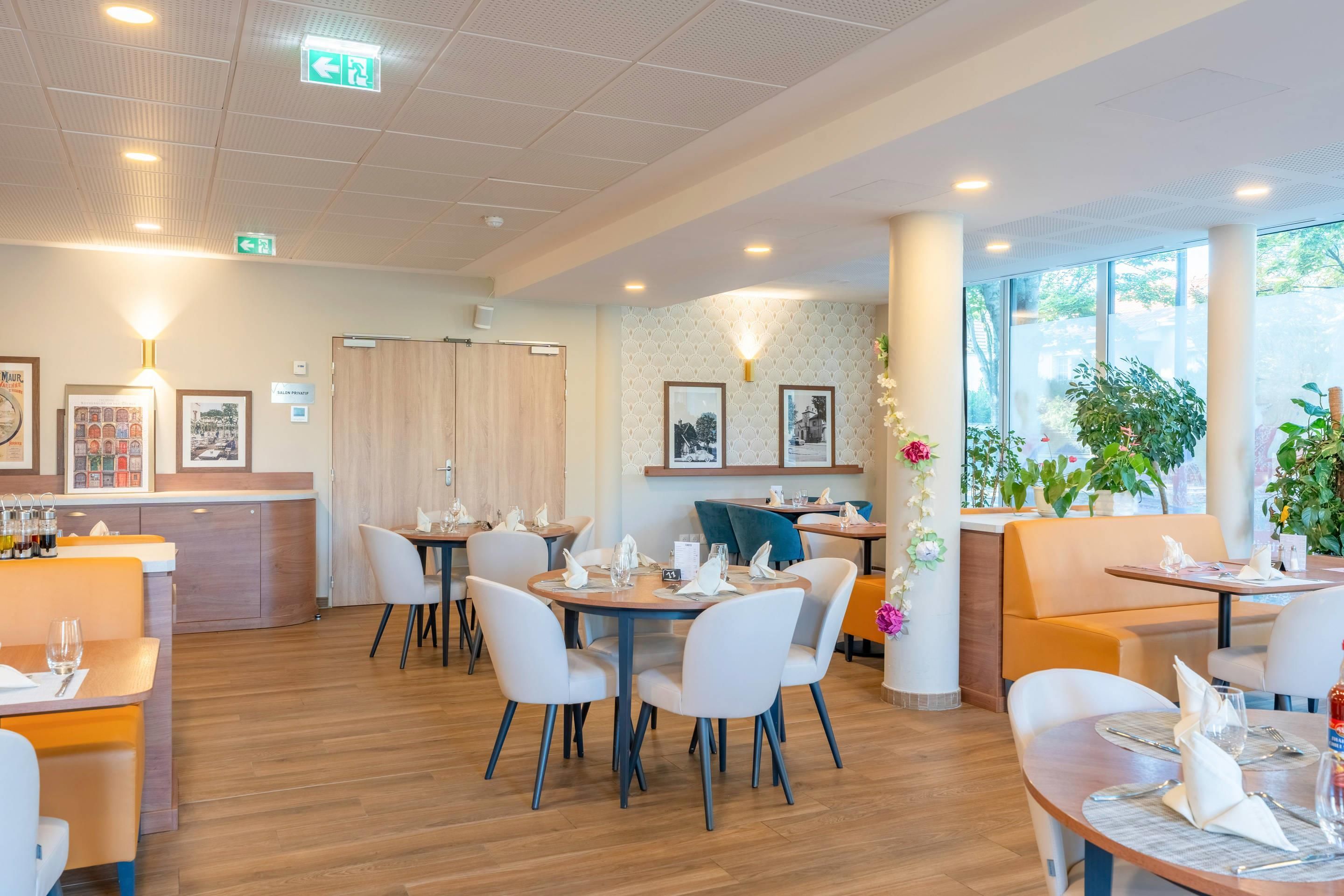 Un restaurant moderne avec des tables rondes, des chaises blanches et un plancher en bois.