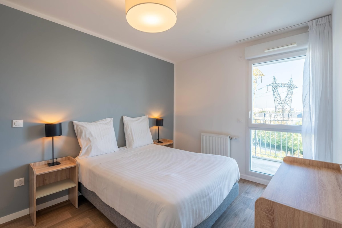 Un dormitorio moderno con una cama grande, dos mesitas de noche con lámparas, una ventana con vistas a líneas eléctricas y un balcón.