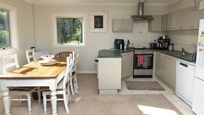 A kitchen with white cabinetry, a wooden dining table, and a coffee machine. - Queenstown House in Arthurs Point (Queenstown)