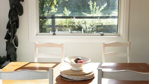 A dining table with two white chairs, a window with a view of greenery, and a plant on the wall. - Queenstown House in Arthurs Point (Queenstown)