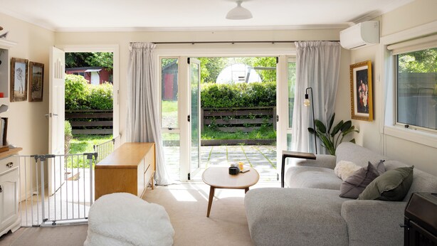 A cozy living room with a sofa, a coffee table, and a white pouf. There is a sliding glass door leading to a garden. - Queenstown House in Arthurs Point (Queenstown)