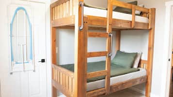 Una cama litera con estructura de madera, colchón verde y escalera metálica.