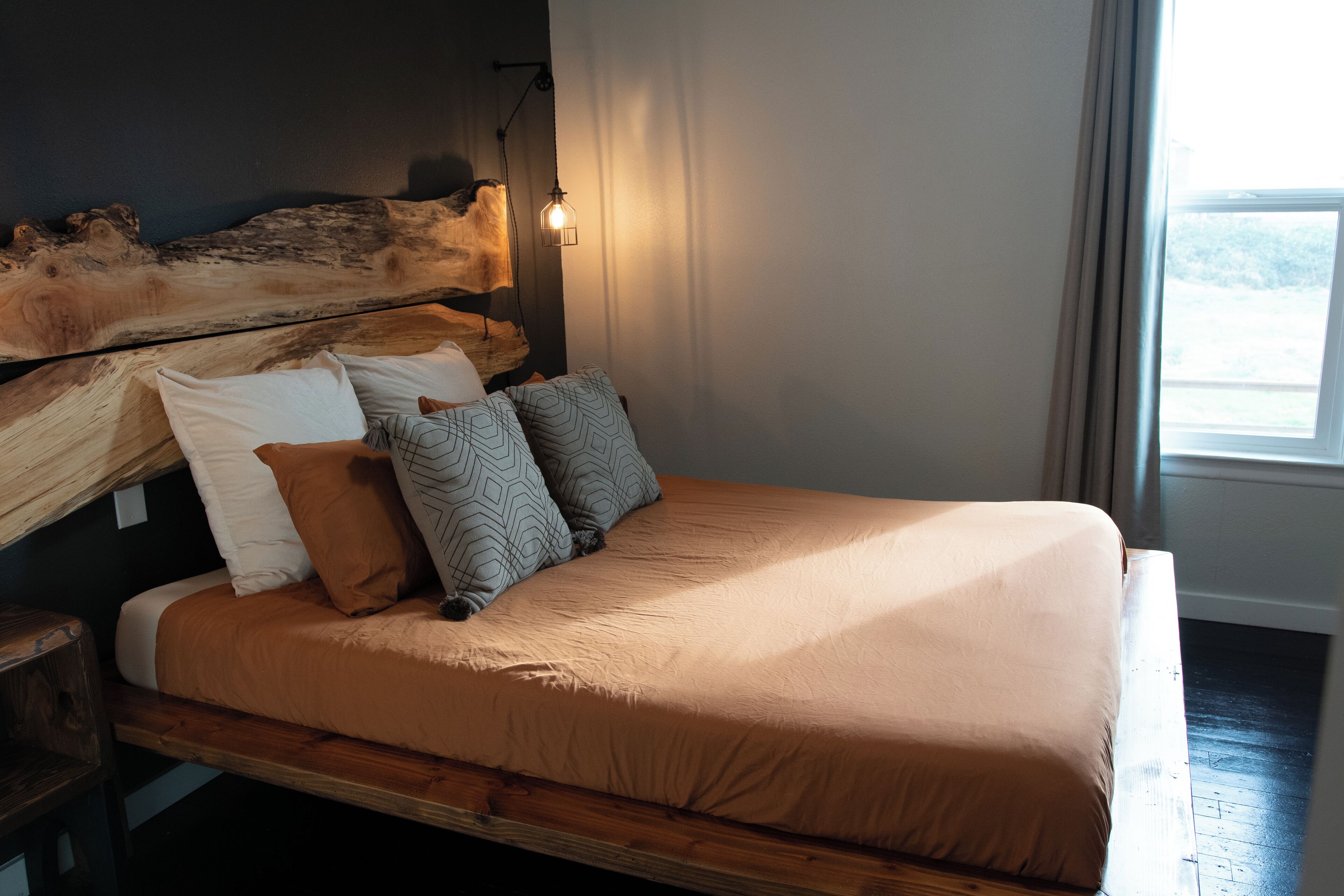 A bed with a wooden headboard, a light fixture, and a window with curtains.