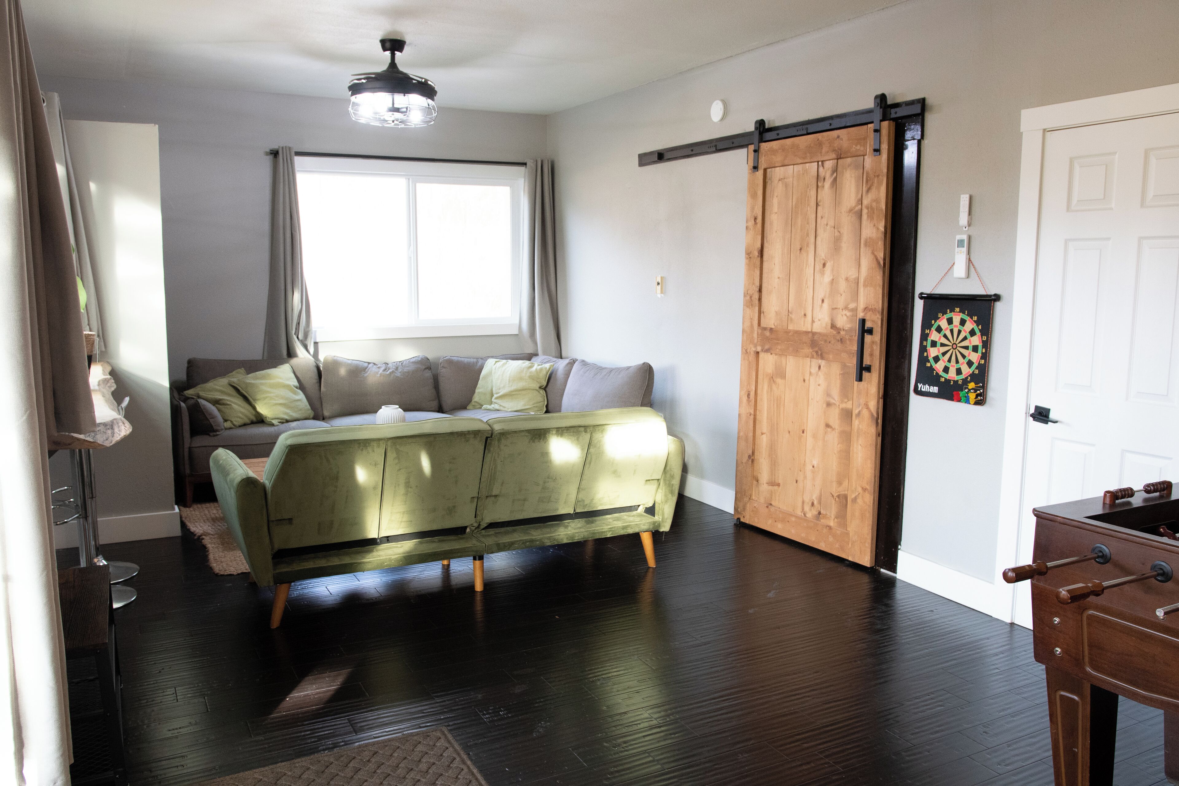 A living room with a green sofa, a wooden sliding door, a dartboard, and a wooden table.