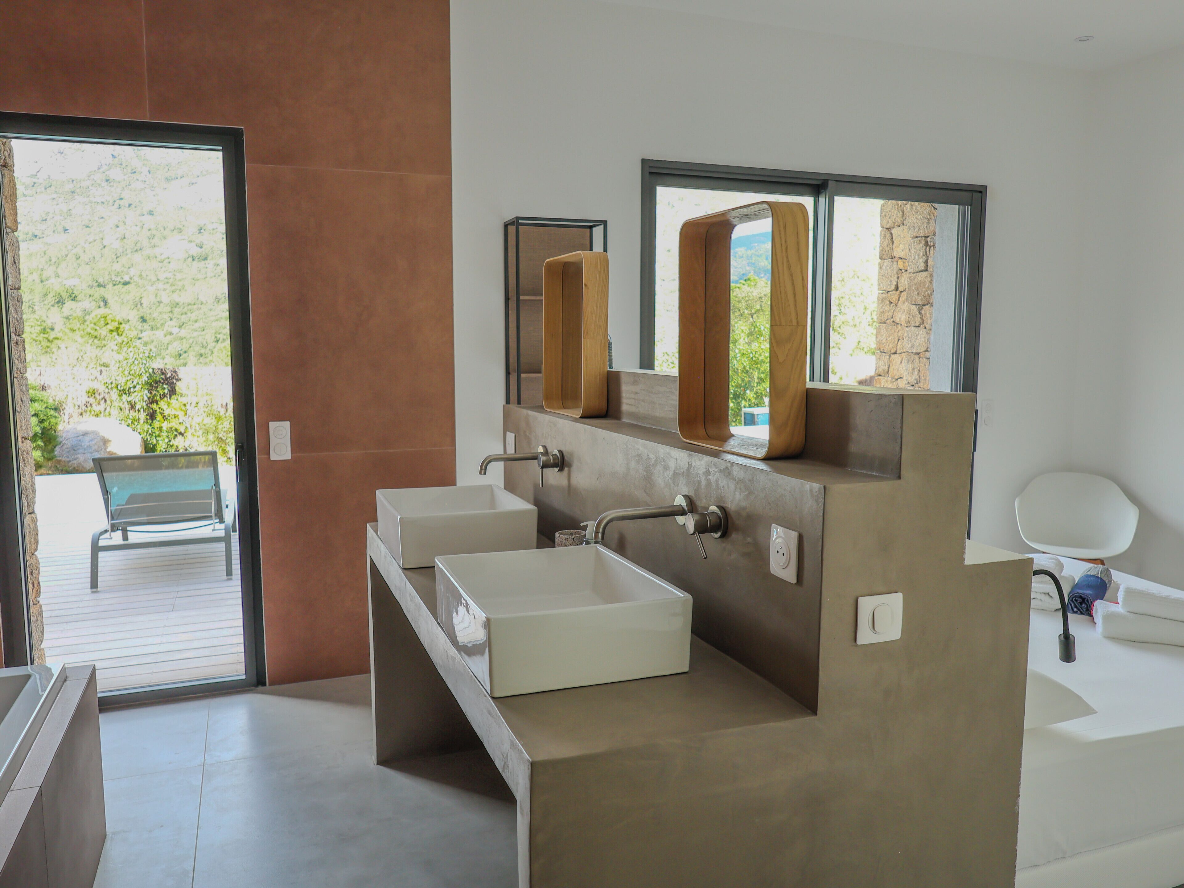 A modern bathroom with a large window, a bench outside, and a view of greenery.