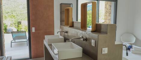 A modern bathroom with a large window, a bench outside, and a view of greenery.