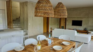Uma sala de jantar moderna com uma mesa de madeira, cadeiras brancas e duas luminárias pendentes de fibra.