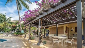 Un espace extérieur abrité comprenant une piscine, des chaises longues et une pergola ornée de plantes à fleurs.