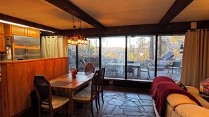 Un intérieur chaleureux avec un sol en pierre, des meubles en bois, une table à manger et une grande fenêtre donnant sur l’extérieur.