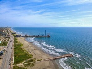 Una carretera costera con una playa y un muelle que se adentra en el mar.
