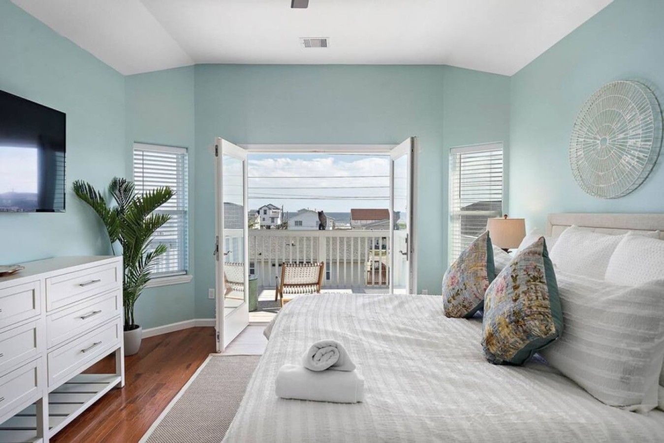 Une chambre à coucher avec un lit, une commode, une plante en pot et une vue sur l’extérieur.