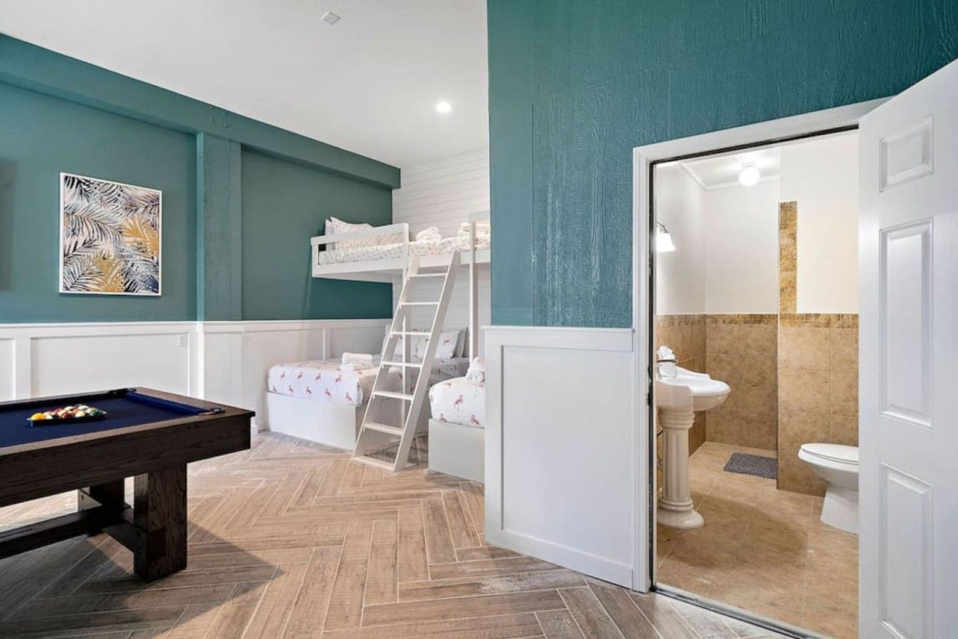 A room with a pool table, bunk beds, and a bathroom with a sink and toilet.