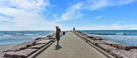 En betongpromenad som leder ner till havet, och en person som går bort från kameran.