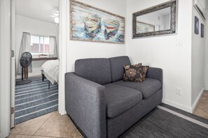 A modern living room with a grey sofa, a floral pillow, a painting of boats, and a mirror on the wall.