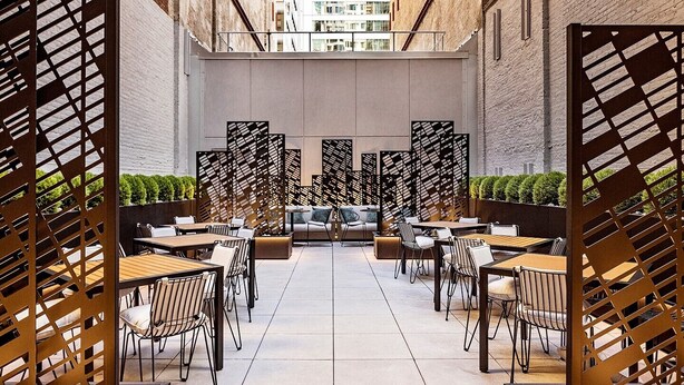 An outdoor dining area with multiple tables and chairs, enclosed by a lattice partition. - High End 1-Bedroom Studio Premier Plus in Midtown Manhattan with many amenities (New York)