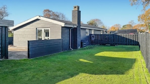 A residential house with a sloped roof, a chimney, and a fenced backyard.