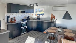 A modern kitchen with dark cabinetry, a built-in oven, a window, and a dining area with stools.
