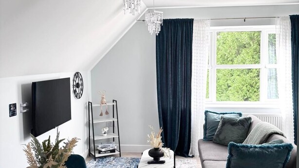 A modern living room with a TV, a chandelier, a sofa, and a dining area with a table and chairs. - Modern Flat • Castle Views & Free Parking (Dover)