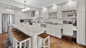 Una cocina moderna con armarios blancos, una isla de granito con taburetes y un horno empotrado.