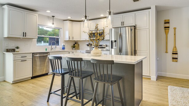 A modern kitchen with white cabinets, stainless steel appliances, and a central island with bar stools. - Stay & Play Tampa- Pool + Mini Golf (Pinellas Park)