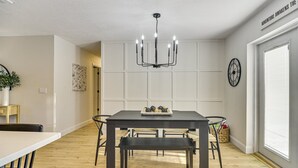 A dining area with a dark wooden table, four chairs, a bench, a chandelier, a clock, and a sign on the wall. - Stay & Play Tampa- Pool + Mini Golf (Pinellas Park)