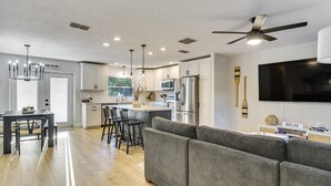 A modern kitchen with white cabinets, a dining area with a table and chairs, a gray sofa, and a ceiling fan. - Stay & Play Tampa- Pool + Mini Golf (Pinellas Park)