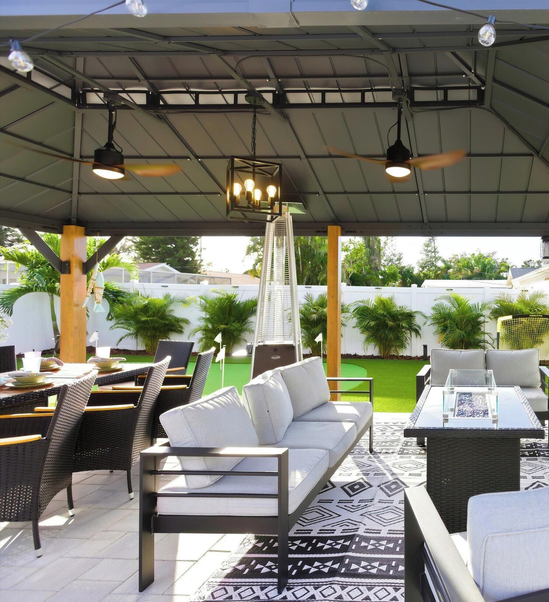 An outdoor patio with wicker furniture, a patterned rug, and a view of a green lawn and white fence.